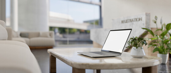 A laptop computer with a white-screen mockup on a coffee table in a modern reception lounge area.
