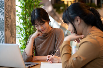 A charming young Asian female college student doing homework with her friend at a cafe.