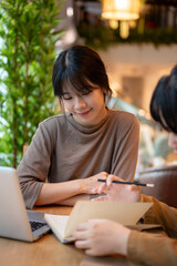 A charming young Asian female college student doing homework with her friend at a cafe.