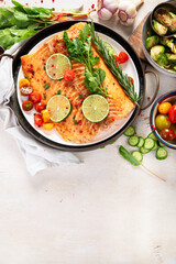 Grilled salmon and vegetables on wooden light background. Dinner table with cooked fish, tomatoes, asparagus