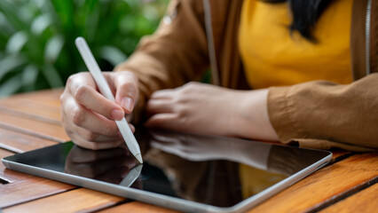 A close-up image of a woman holding a stylus pen, drawing or writing on her digital tablet.