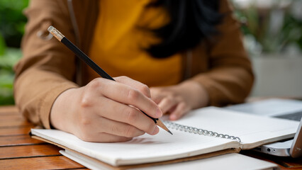 A close-up image of an Asian woman holding a pencil, writing something in her notebook.