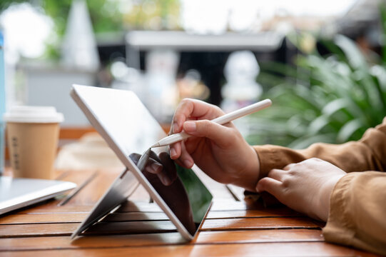 A side view image of a woman drawing or writing something on her digital tablet with a stylus pen.