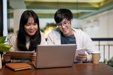 Obraz premium Two young Asian college student friends are working on a co-project together at a cafe.