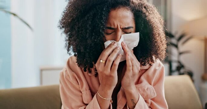Black woman, sick and blowing nose with tissue on sofa for illness, virus or infection in living room. Young African or female person with cold, flu or sneeze from sinus, allergy or disease at home