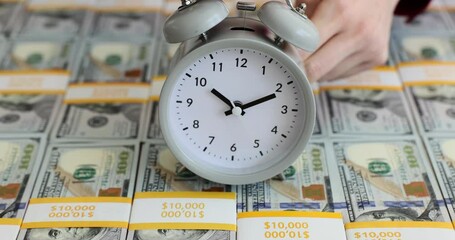 Woman places alarm clock on surface with dollar bills packs - Powered by Adobe