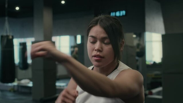 Close-up shot of face and hands of young female boxer performing fast-paced shadowboxing routine at busy gym, perfecting punch, jab, lunge, hook, uppercut maneuvers