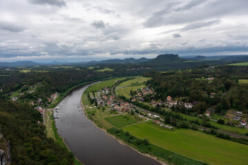 A river runs through a town with houses and a bridge. The sky is cloudy and the water is dark