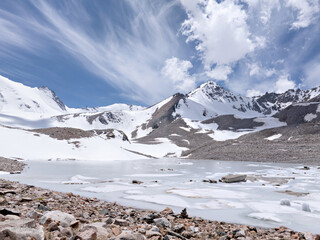 Lake in the valley among snow covered mountains. Ski resort in the mountains. Clouds over peaks....