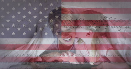 American flag and constitution text against caucasian girl kissing her mother under a blanket