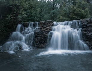 Fototapeta premium serene waterfall flowing over rocks surrounded by lush green forest