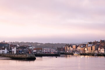 Naklejka premium Picturesque view of Whitby harbor at sunset with historic buildings along the waterfront.