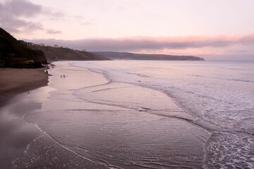 A serene beach scene at sunset with gentle waves and distant cliffs