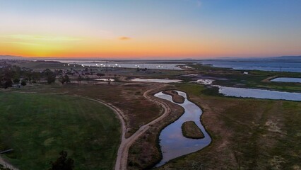 A scenic aerial view of a coastal wetland at sunset with winding paths and water channels