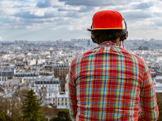 Obraz premium A man wearing a red cap and headphones, overlooking the cityscape from a high vantage point.