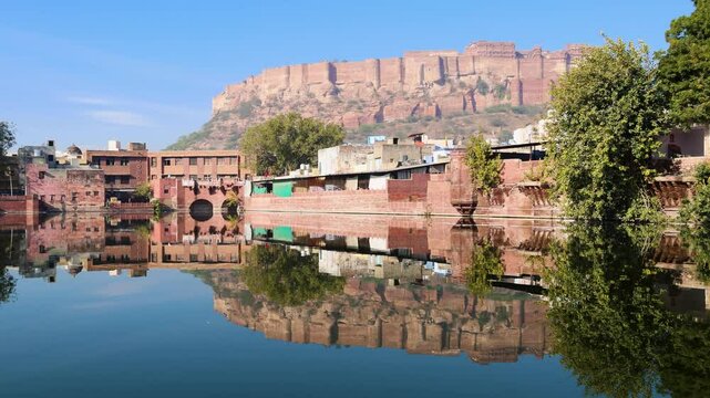 pristine calm lake with reflection of historical mehrangarh fort and houses around at morning video is taken at Gulab sagar talab jodhpur rajasthan india.