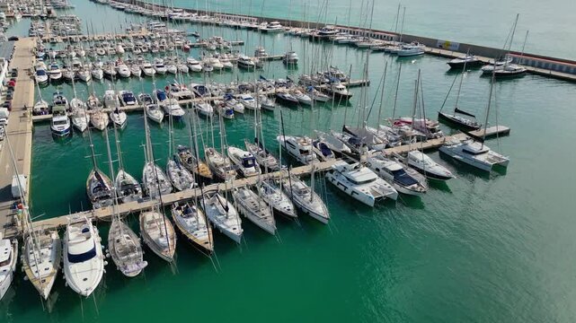 The coast and port of ginesta in barcelona with docked boats in clear blue water, aerial view