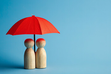 Red toy umbrella and wooden dolls isolated on blue background, symbolizing insurance coverage and protection