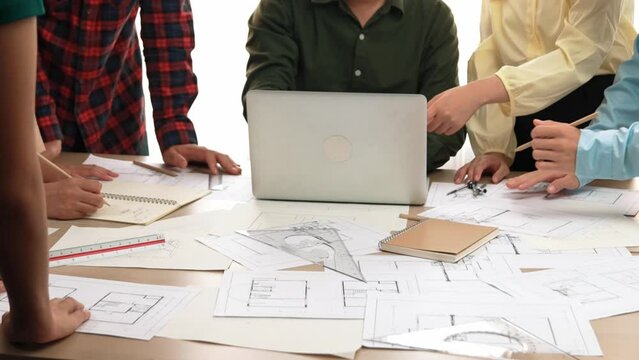 Architect and safety engineer discussion about building blueprint displaying on laptop on table with architectural document and wooden block scatter around at modern office. Closeup. Delineation.