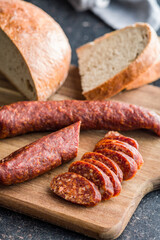 Sliced smoked salami sausage on wooden cutting board on black table.