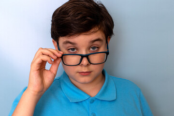 Fototapeta premium A close-up of a boy with glasses on a blue background, who looks over his glasses at the camera