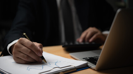 Obraz premium Businessman writing on financial charts, using calculator. Detail-oriented work in finance, accounting. Perfect for business management, financial planning, corporate presentations.