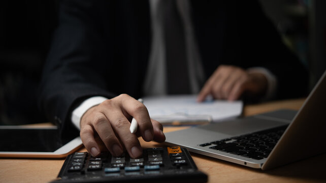 Businessman using calculator, writing on paperwork. Financial analysis, accounting, Ideal for finance, accounting, business management visuals. Professional atmosphere. - Powered by Adobe
