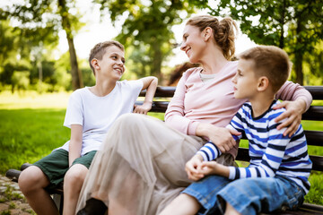 Fototapeta premium Happy mother is sitting with her sons on bench in park. They are having fun together.