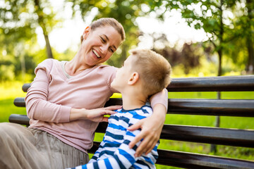 Fototapeta premium Happy mother is sitting with her son on bench in park. They are having fun together.