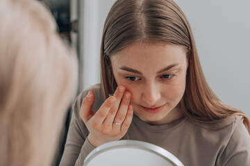 Young woman trying to insert contact lens in eye at clinic