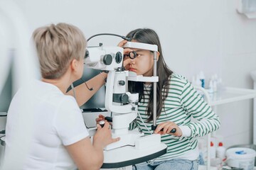 Ophthalmologist using optical instrument for checking girl's eyes
