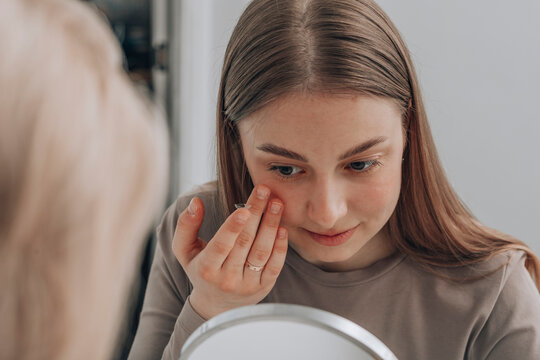 Young woman trying to insert contact lens in eye at clinic
