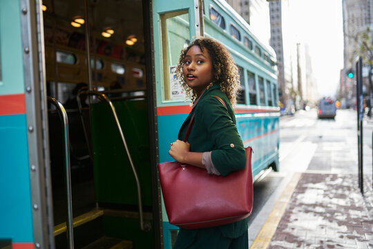 Beautiful young businesswoman with purse boarding bus in city