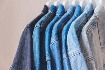 Many denim trucker jackets on hangers, close up view. Different shades of jean textile colors.