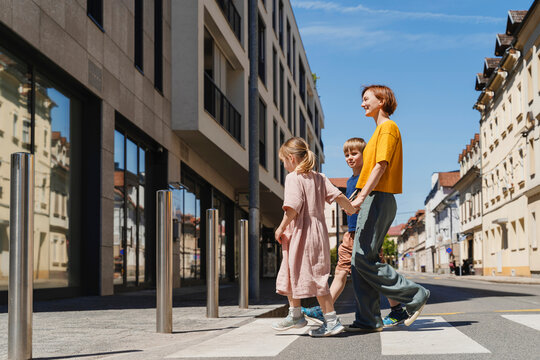 Mother crossing street with son and daughter near buildings on sunny day