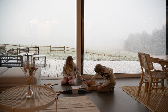 Siblings playing by large window at home in winter