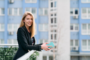 Fototapeta premium Blonde Businesswoman in Black Suit Using Smartphone on Break in Modern Urban Environment.