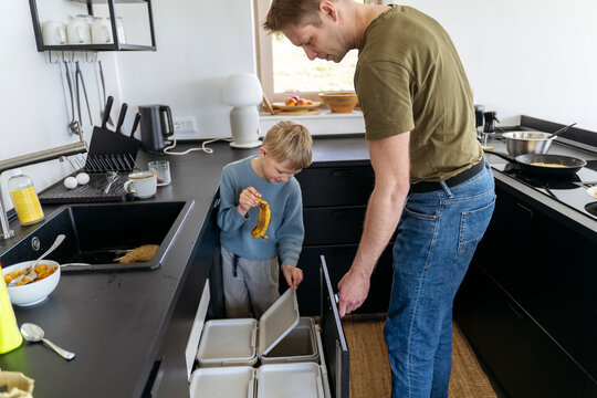 Father looking at son throwing banana peel in trash can