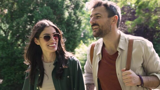 Young woman and man walking in city park holding hands and hugging. Young couple in love walk through the park enjoying sunny and nice weather after work day is over. Simple living concept.