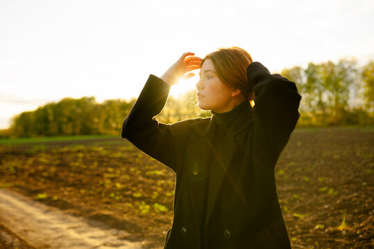Thoughtful woman with hand in hair standing on dirt road near field