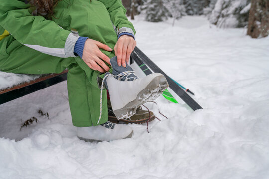 Woman tying shoelace sitting on bench in winter at forest