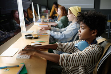 Selective focus shot of African American boy sitting at desk in Computer Science classroom developing code