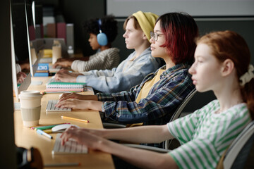 Selective focus shot of Asian teen girl and her multi-ethnic classmates typing on modern computers during coding class at school