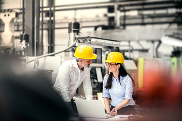 Two project managers standing in modern industrial factory. Manufacturing facility with robotics,...