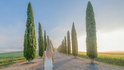 A blonde haired woman stands by a row of Cypress trees in Tuscany, Italy 