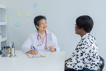 Fototapeta premium Asian senior female specialist consulting with African American woman in medical clinic or hospital. Doctor gestures while explaining using technology laptop, medical health care diagnosis concept