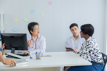 Young Caucasian doctor taking blood pressure of African American patient woman in clinic. Asian senior female advisor observation, Specialists collaboration diagnosis in medical health care hospital