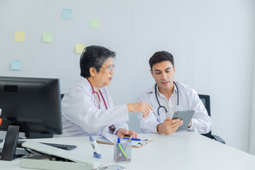 Professional team senior doctor woman and young specialists wearing white coats with stethoscope consulting, examining illness health symptoms report using technology tablet device in modern hospital