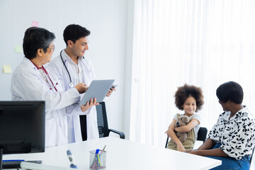 Fototapeta premium Professional collaboration child's health team and patient in hospital. Caucasian pediatrician male using stethoscope diagnosis. Family-oriented health care with senior Asian female and young doctor