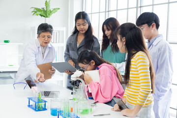 Group of students in science class using laptops and microscopes, conducting experiments. Young diverse pupils focused on research and senior teacher supervision. educations and back to school concept